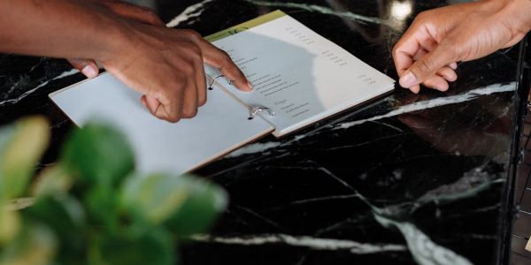 Hands pointing at menu on black marble counter inside a shop.