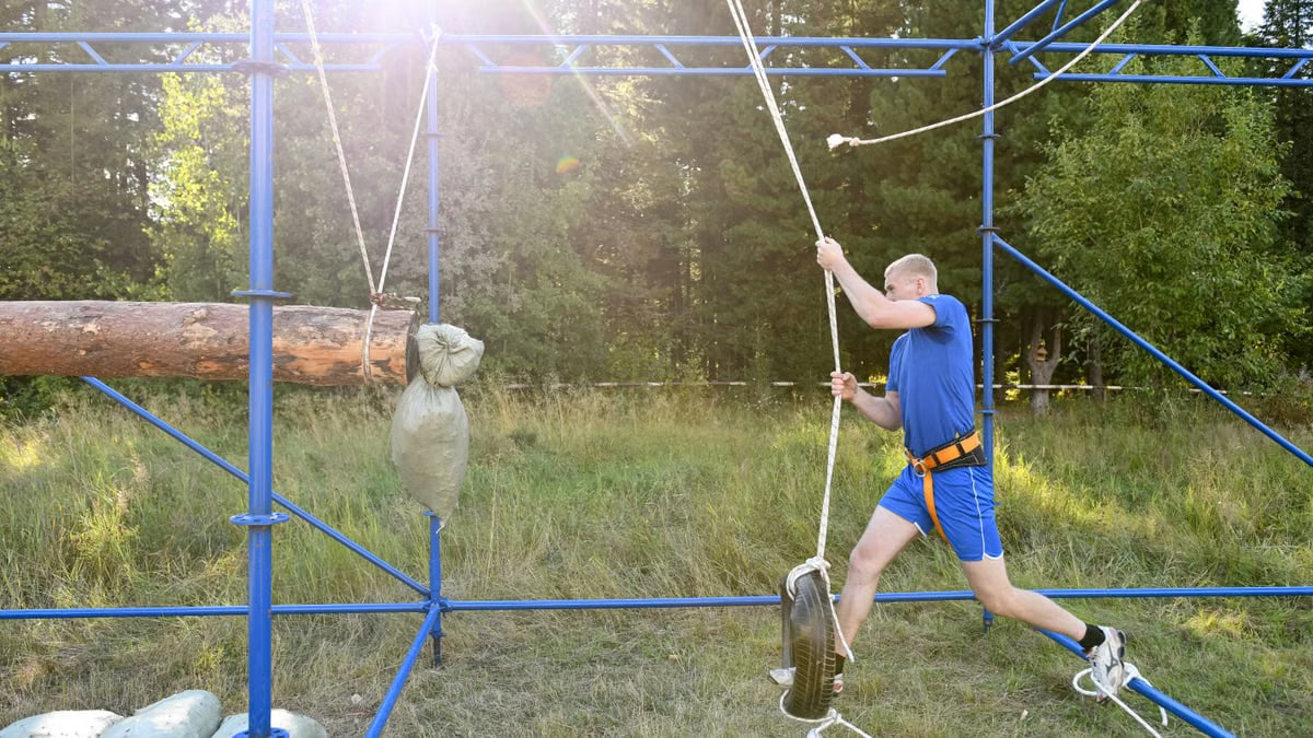 Man mastering an outdoor obstacle course with ropes and tires, showcasing strength and agility.